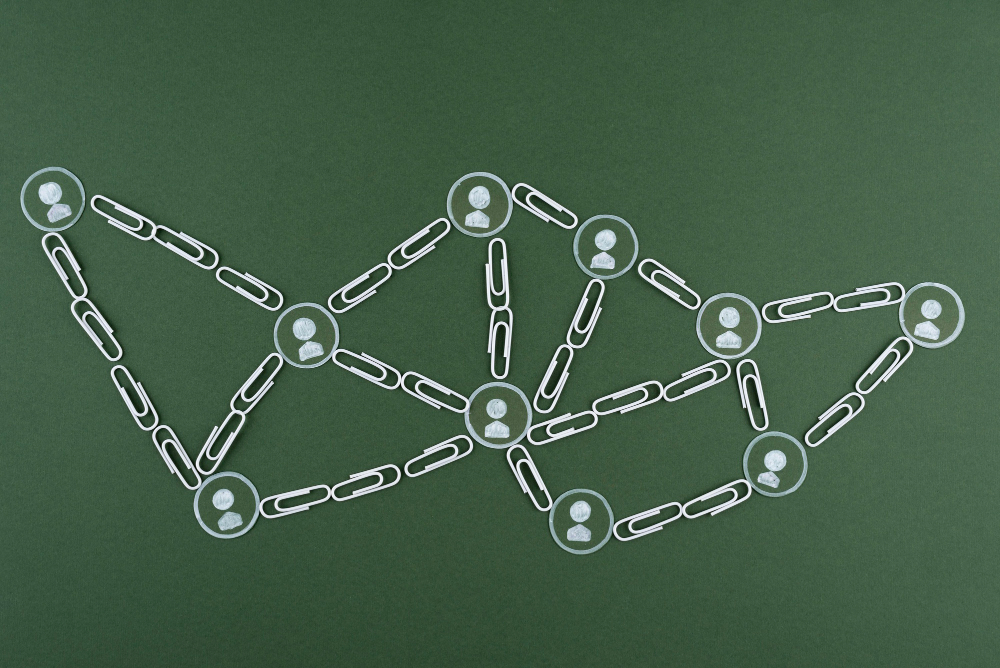 Visual representation of a decentralized network using paper clips and circular icons with user avatars on a green background, symbolizing blockchain or distributed systems.