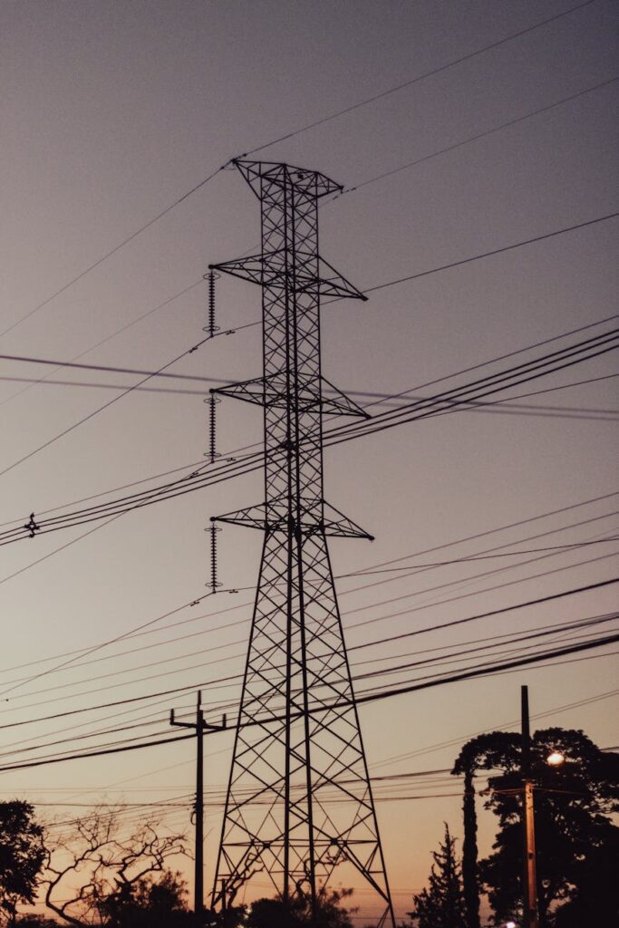 Silhouette of high-voltage power lines and an electrical substation against a dramatic sunset.