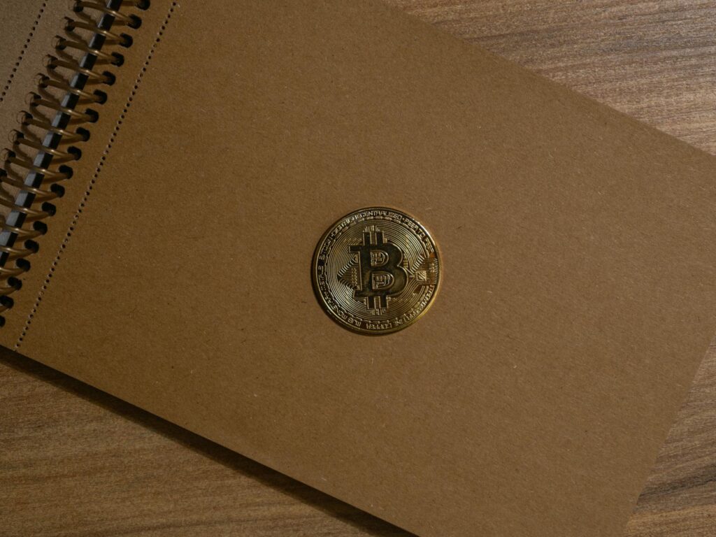 A close-up photograph of a physical gold Bitcoin coin resting on a textured black surface.