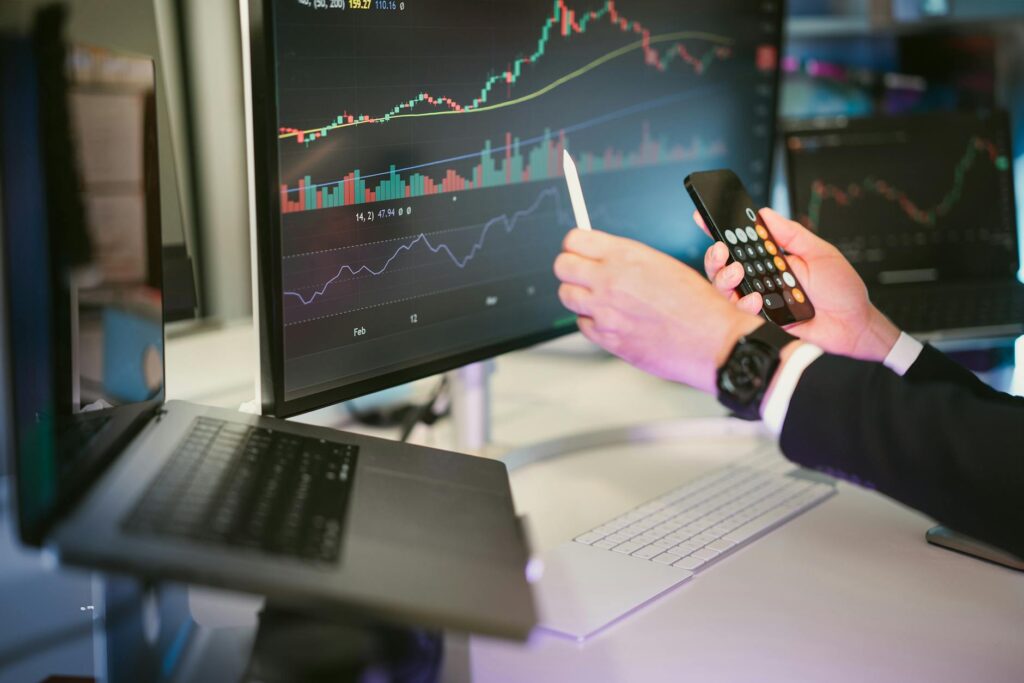 A trader's hands on a keyboard with complex cryptocurrency price charts displayed on a multi-monitor setup.