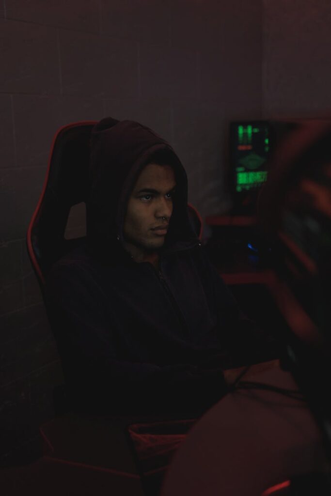 A silhouette of a person in a dark room surrounded by computer screens showing lines of code, illustrating data analysis.