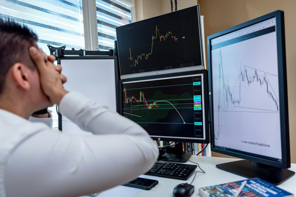 An investor thoughtfully analyzing complex charts and graphs on multiple computer monitors in a home office.