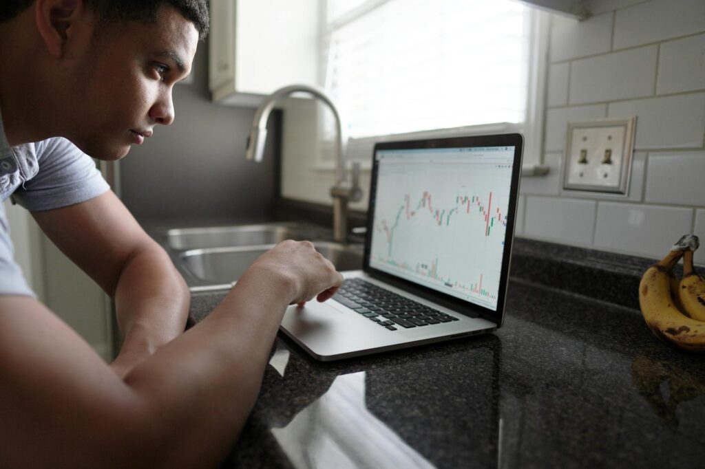 A close-up shot of a person's hands on a laptop keyboard, with financial charts visible on the screen.