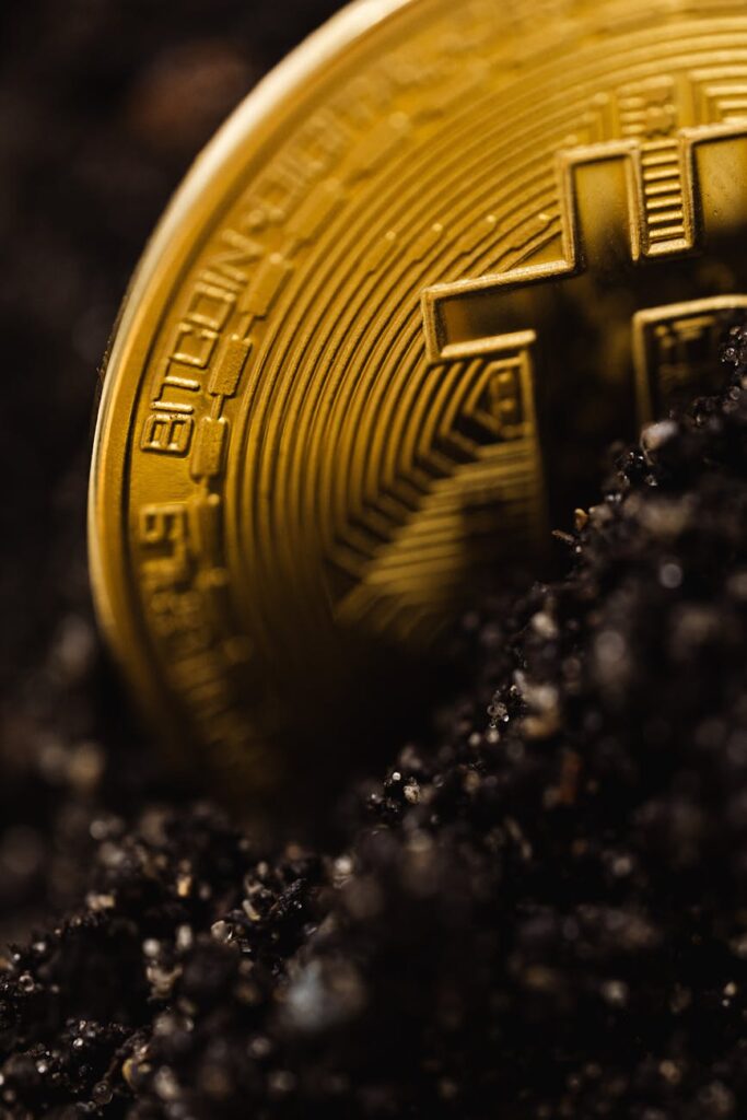 A single physical gold Bitcoin coin resting on a dark, textured surface.