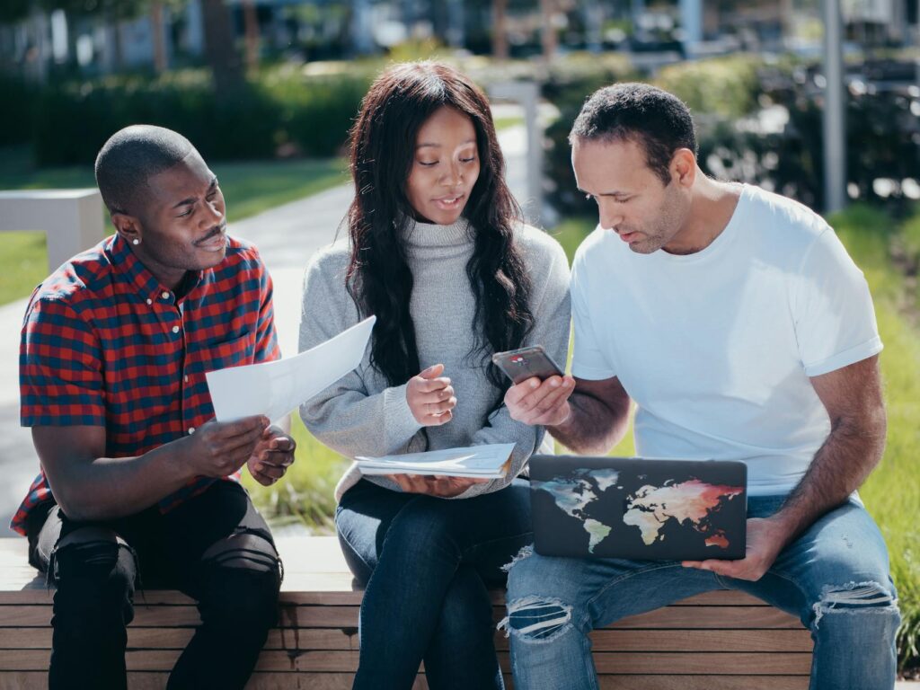 A user's hands holding a smartphone displaying a two-factor authentication app with a code, with a laptop in the background.