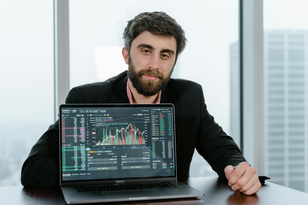 A person's hands pointing at a candlestick chart with technical indicators displayed on a bright laptop screen.