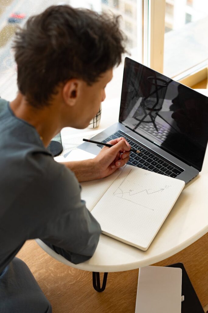 A trader's hands typing on a laptop displaying cryptocurrency market data and graphs.