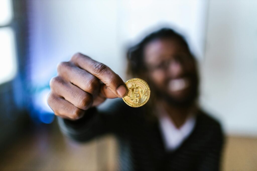 A person's hand holding a shiny, gold physical bitcoin, representing the tangible aspect of digital currency.
