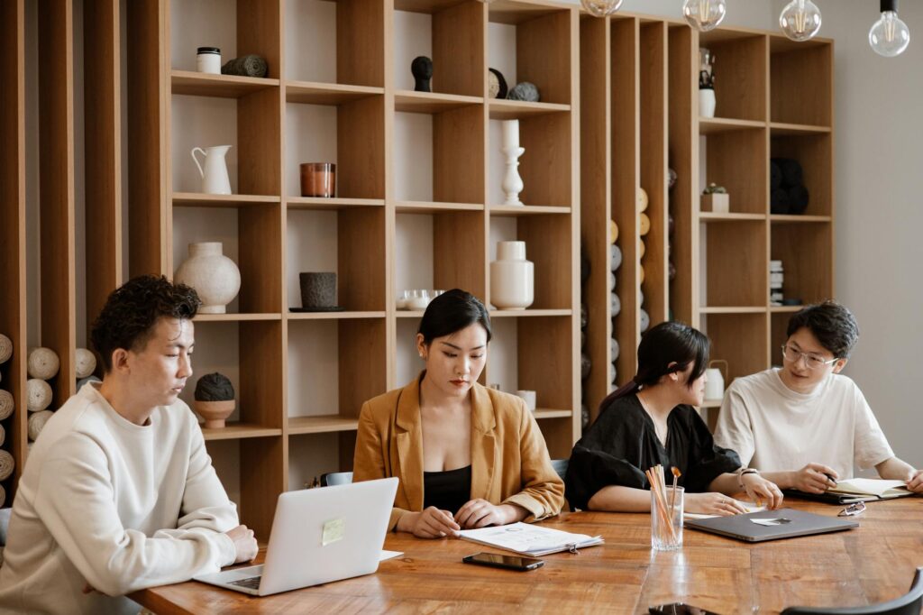 A team of diverse professionals collaborating around a table, pointing at financial data on a monitor.