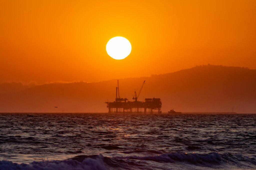 An offshore oil rig silhouetted against a dramatic orange sunset, representing the energy sector's influence.