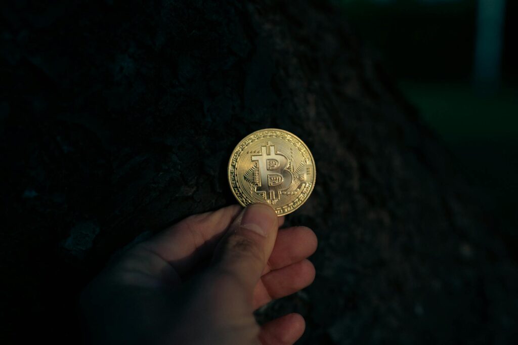 A close-up photograph of a physical Bitcoin token glowing with a golden light against a black backdrop.