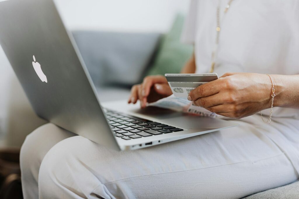 A person's hand holding a physical bitcoin in front of a laptop displaying a crypto chart.
