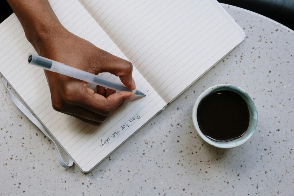 An overhead shot of a person's hand meticulously writing down a 12-word crypto seed phrase onto a notepad.