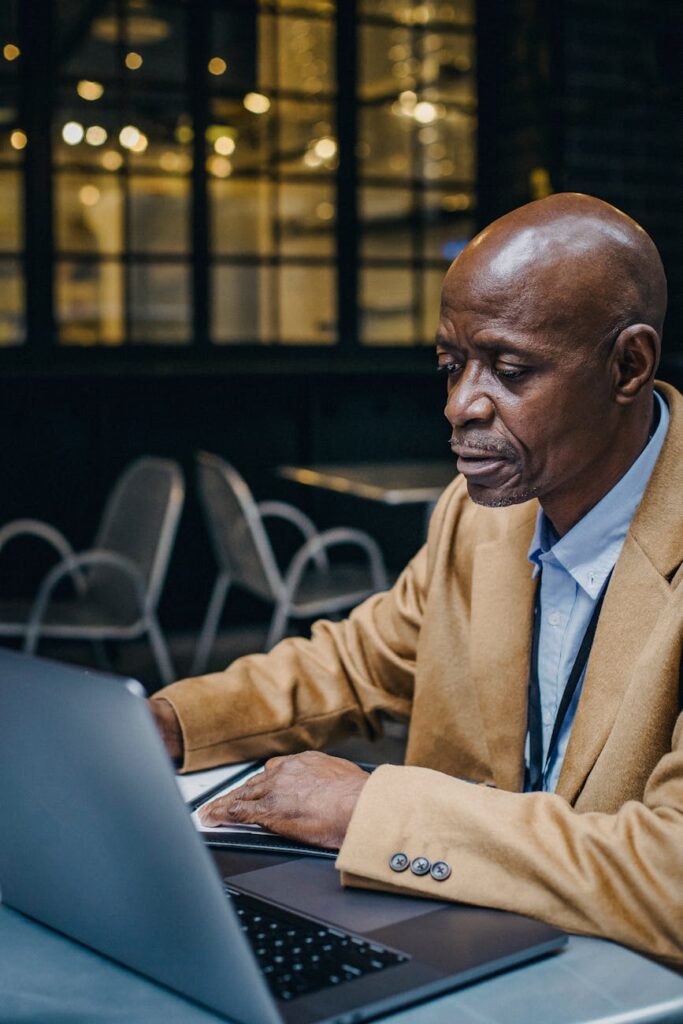 A person focused on their laptop screen while sitting at a table in a bustling, modern coffee shop.